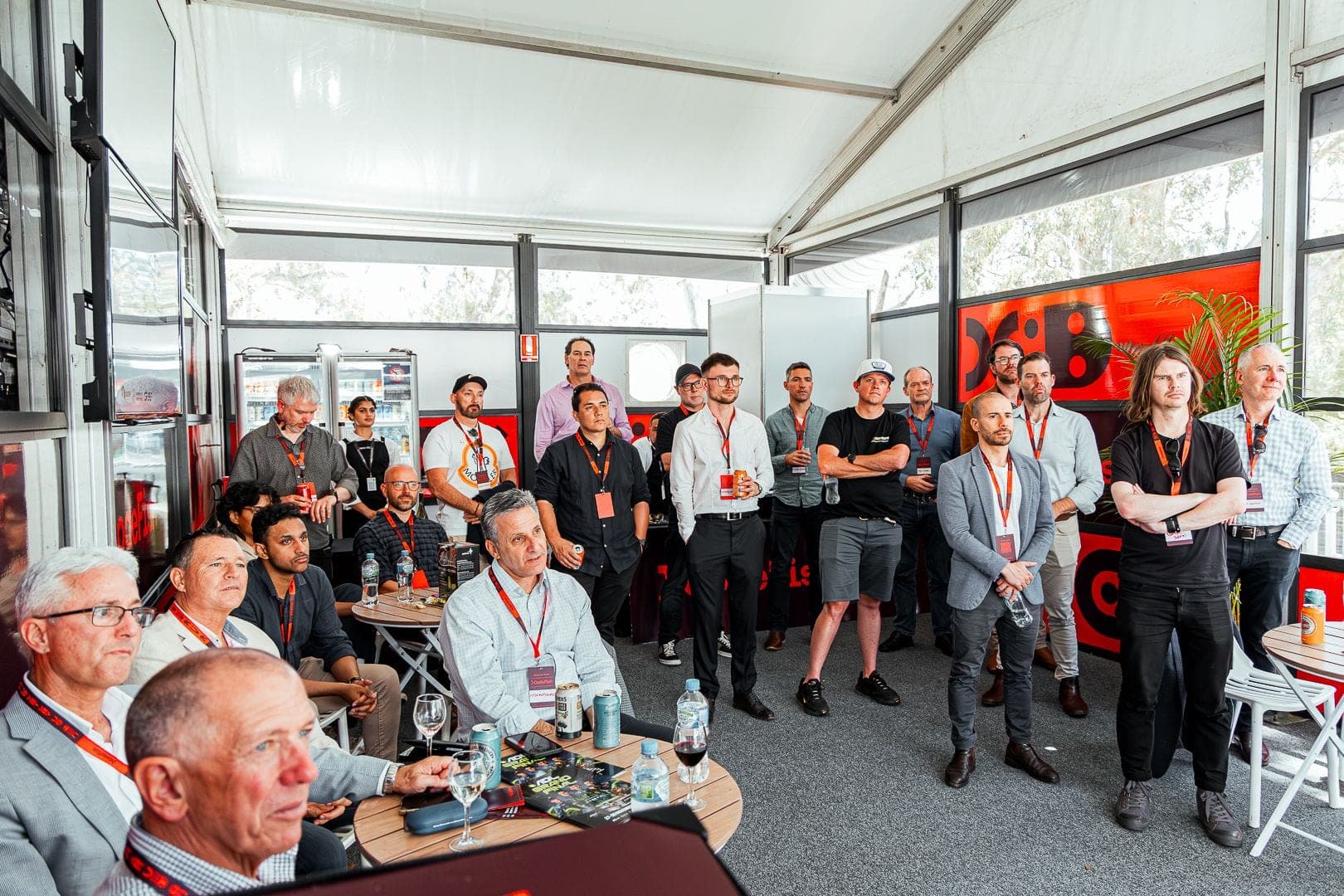 A crowd of guests in a branded marquee listening to a presentation at a motorsport event