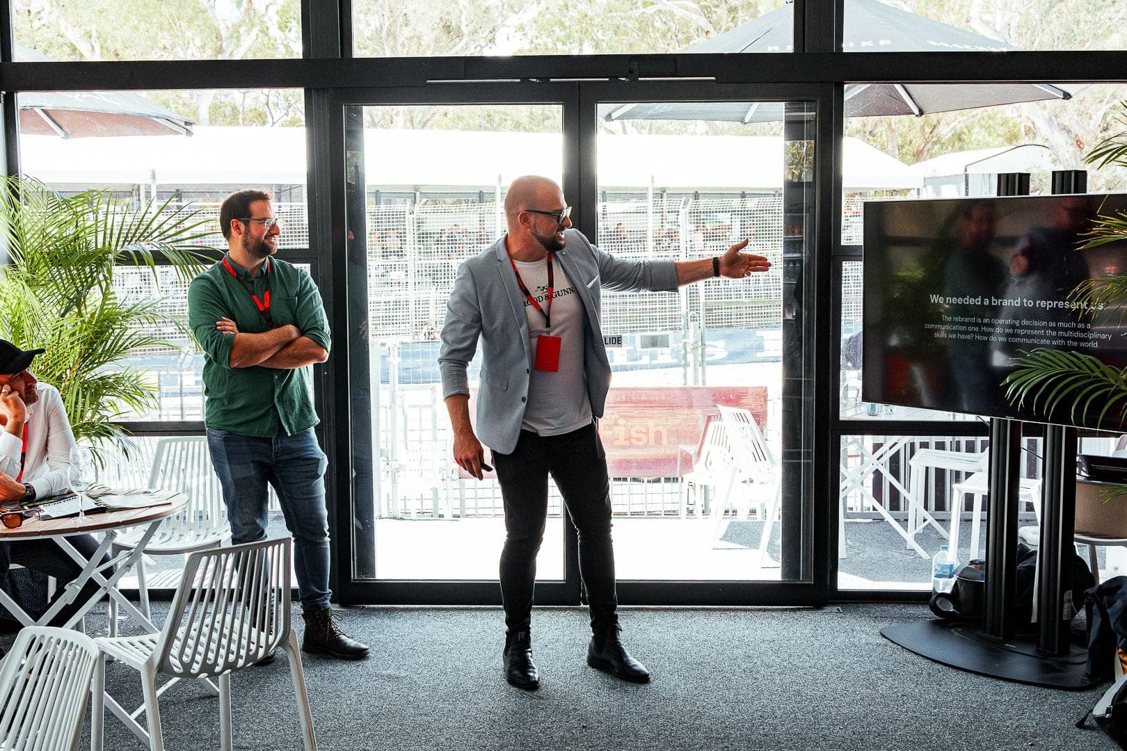 A presenter gesturing to a screen while a colleague listens in a branded marquee