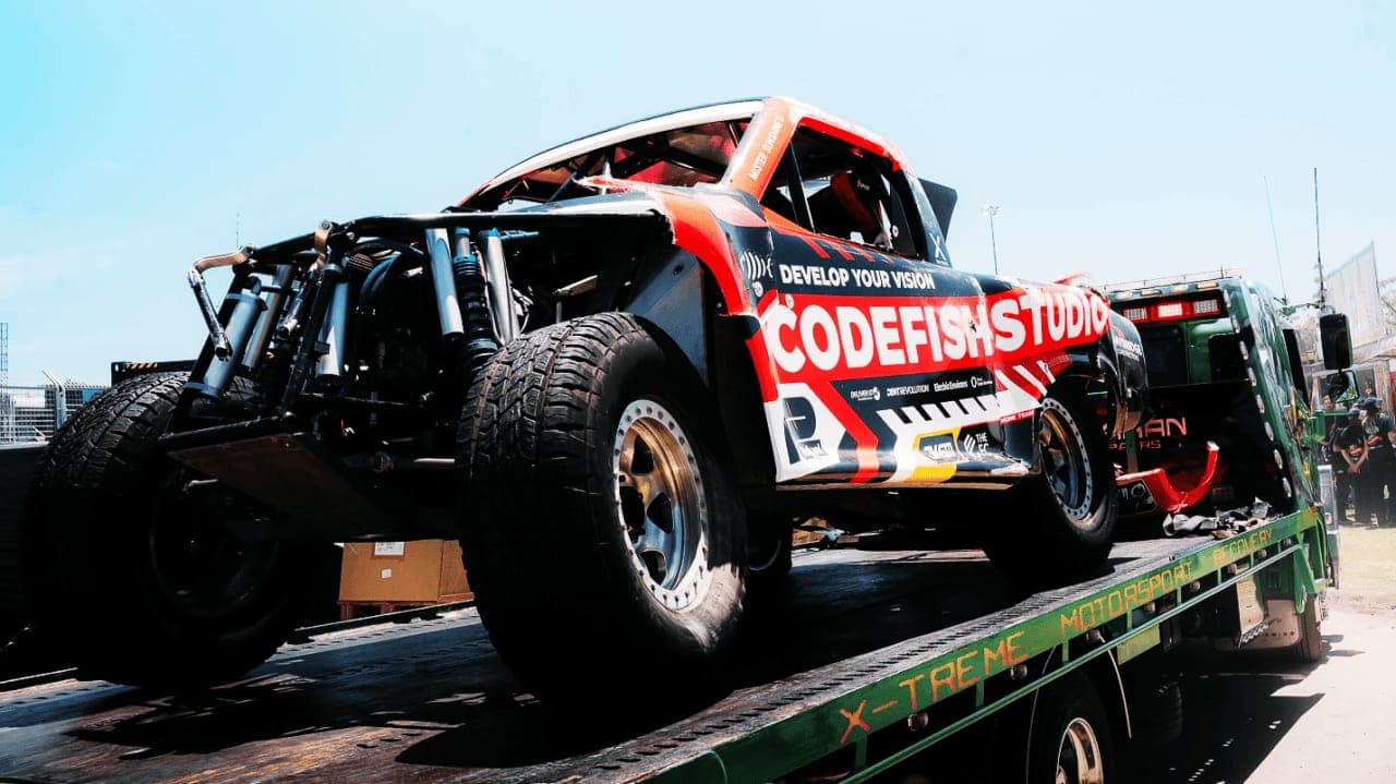 CodeFish Studio race truck loaded onto a motorsport transporter flatbed in the pits