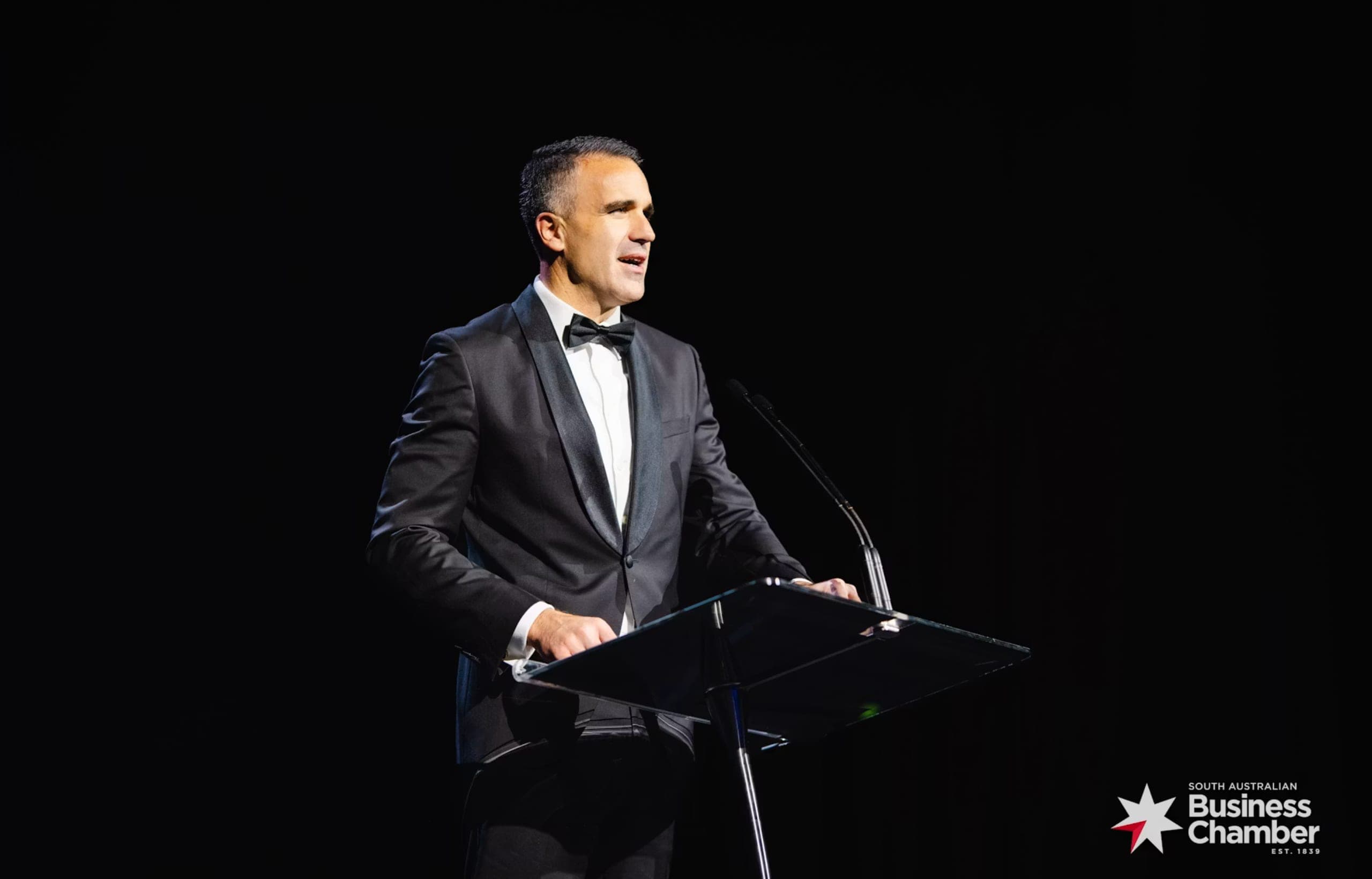 A speaker in black tie addressing the Business and Export Awards audience from a lectern