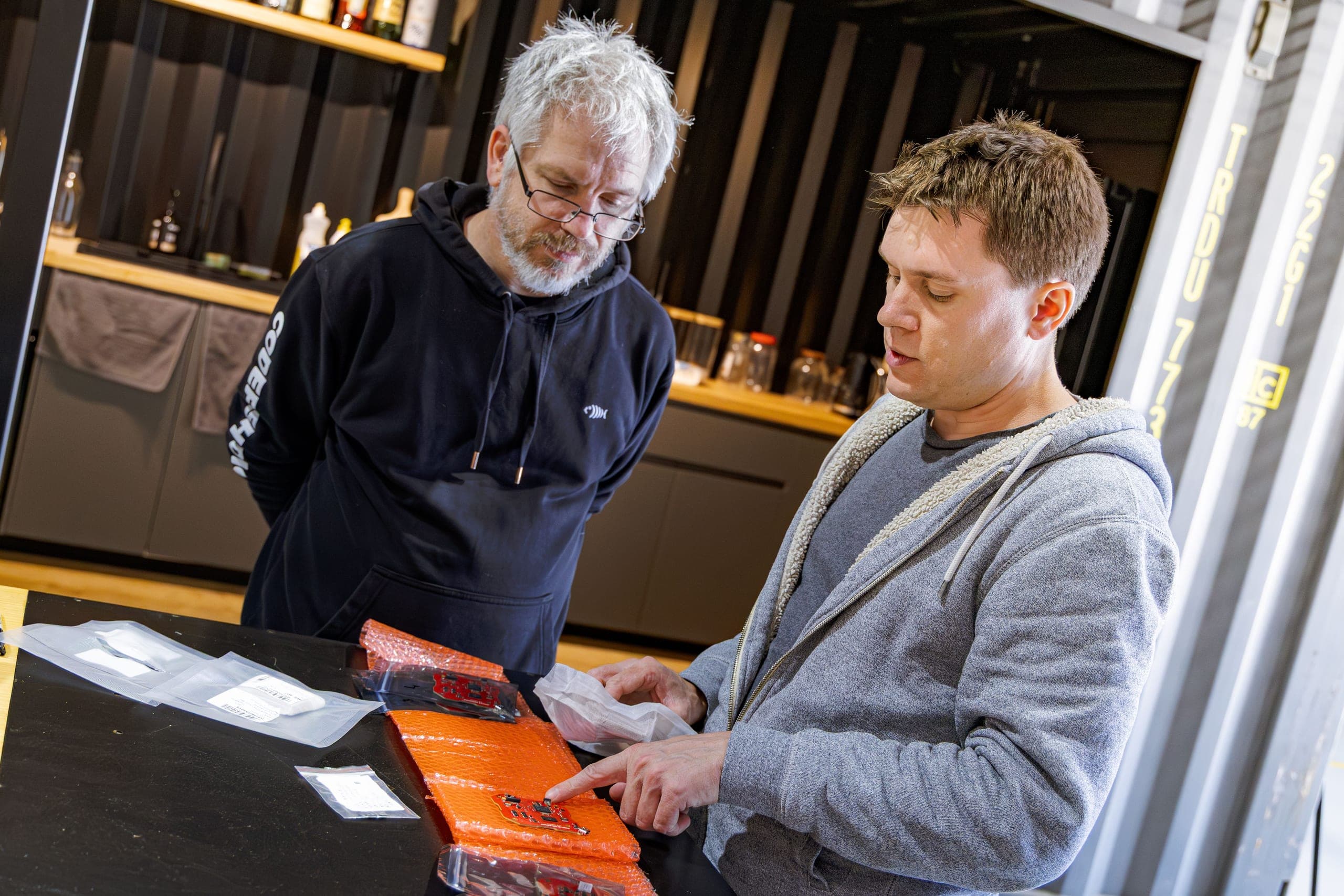Two people looking at a small circuit board on a workbench