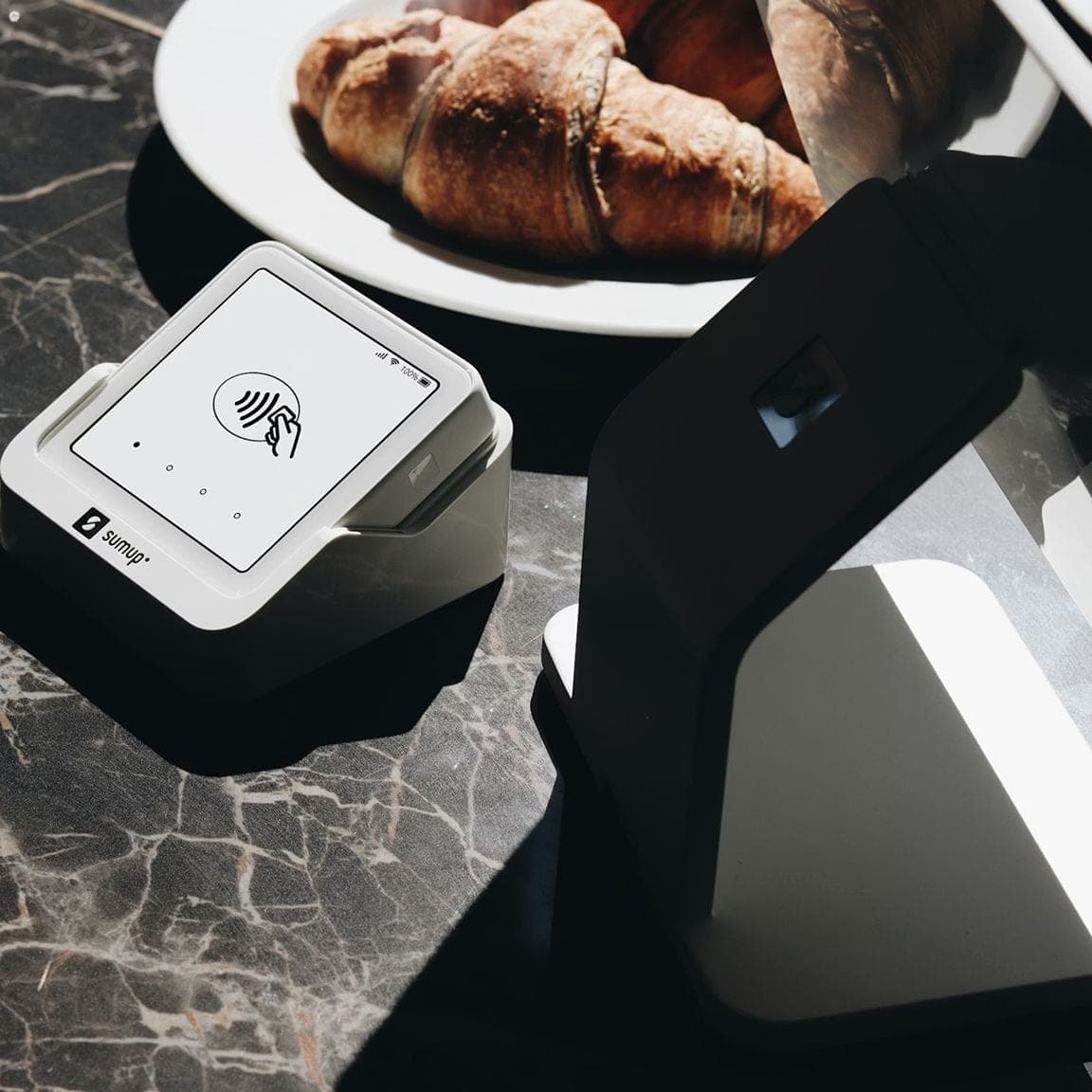 Card payment terminal on a marble table next to a plate of croissants