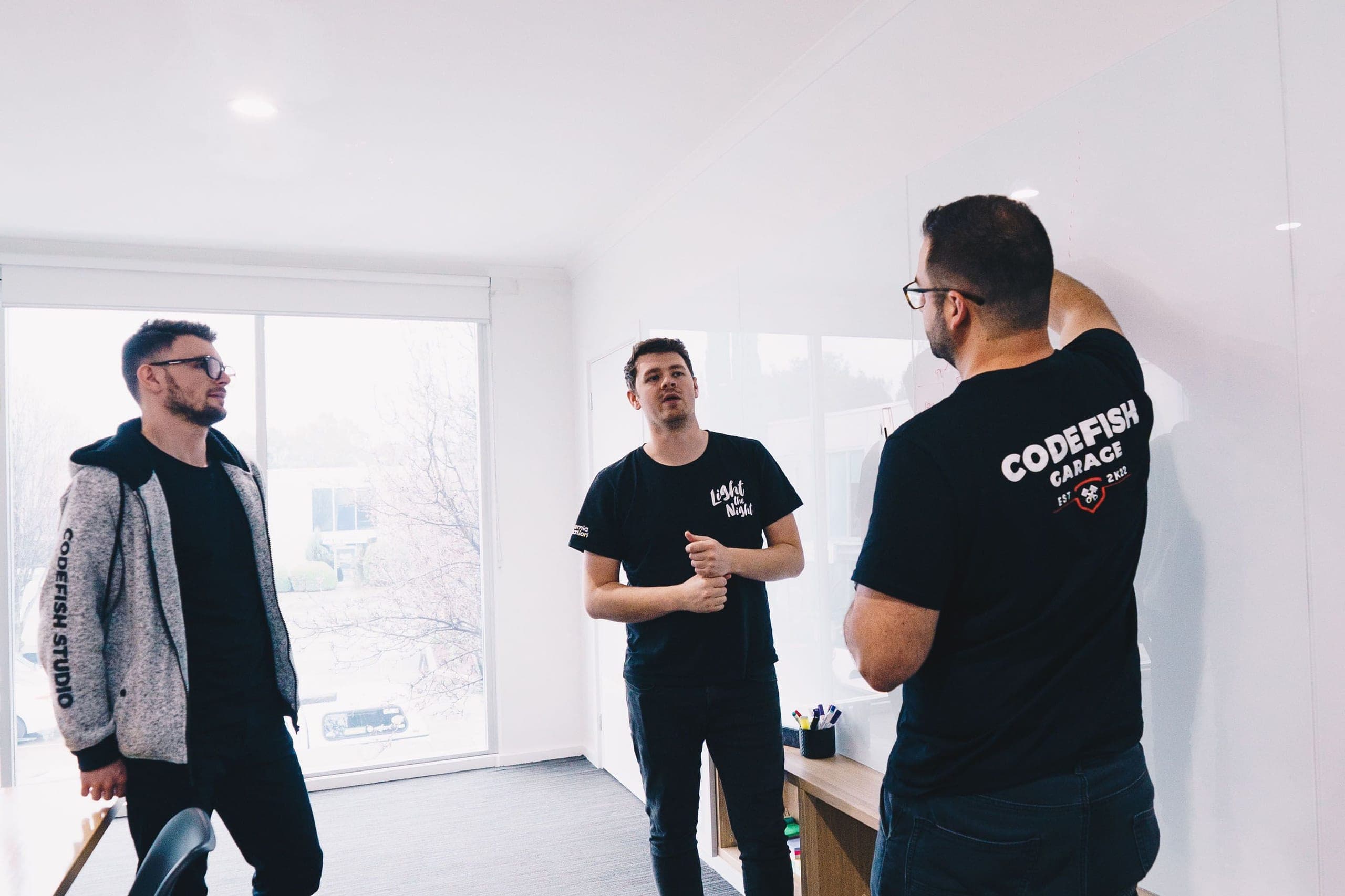 Three team members in CodeFish shirts talking in a whiteboard scoping session