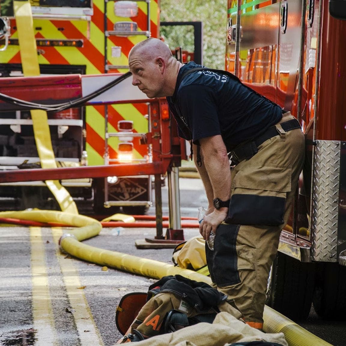 Firefighter pausing beside fire trucks and hoses on a street
