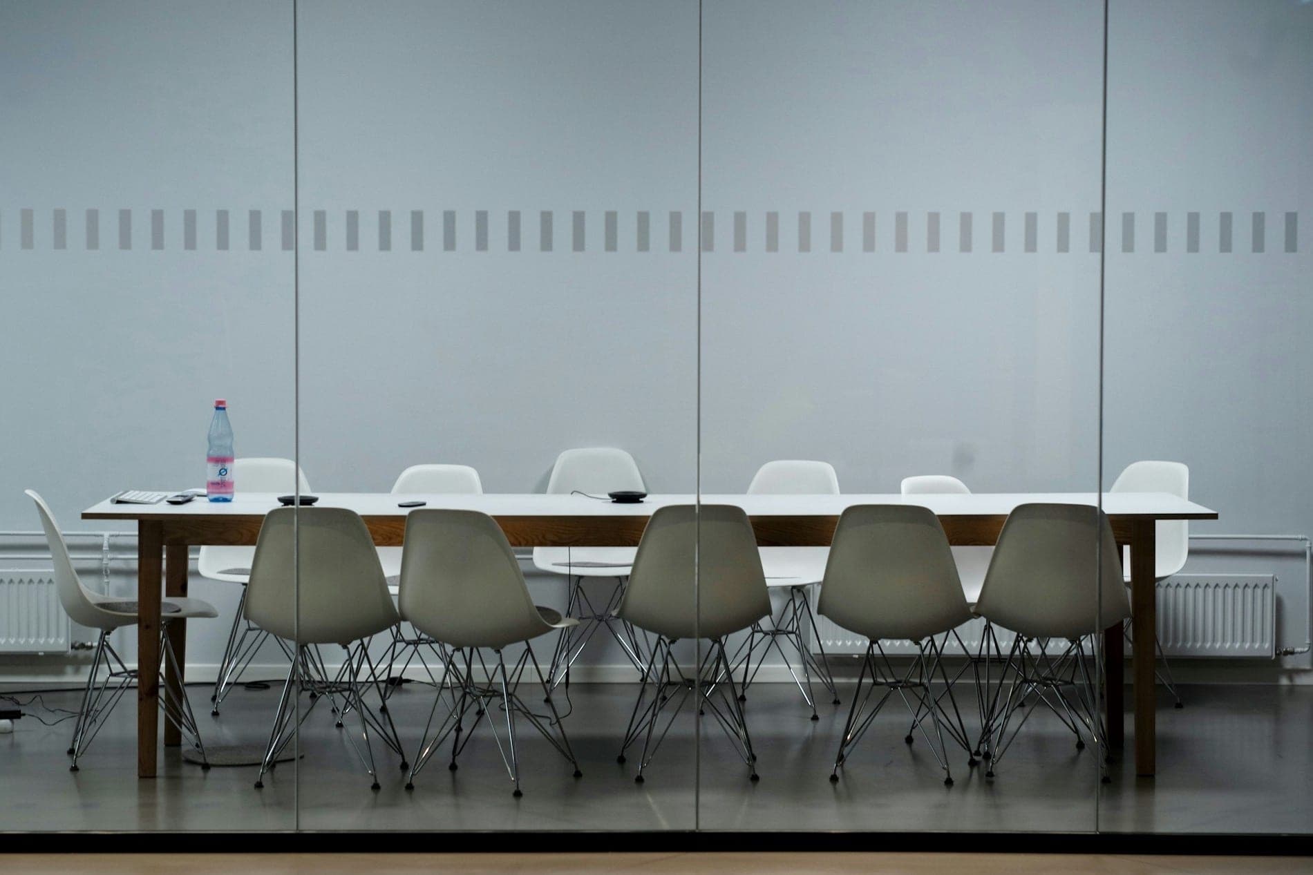 An empty boardroom with a long table, seen through a glass wall