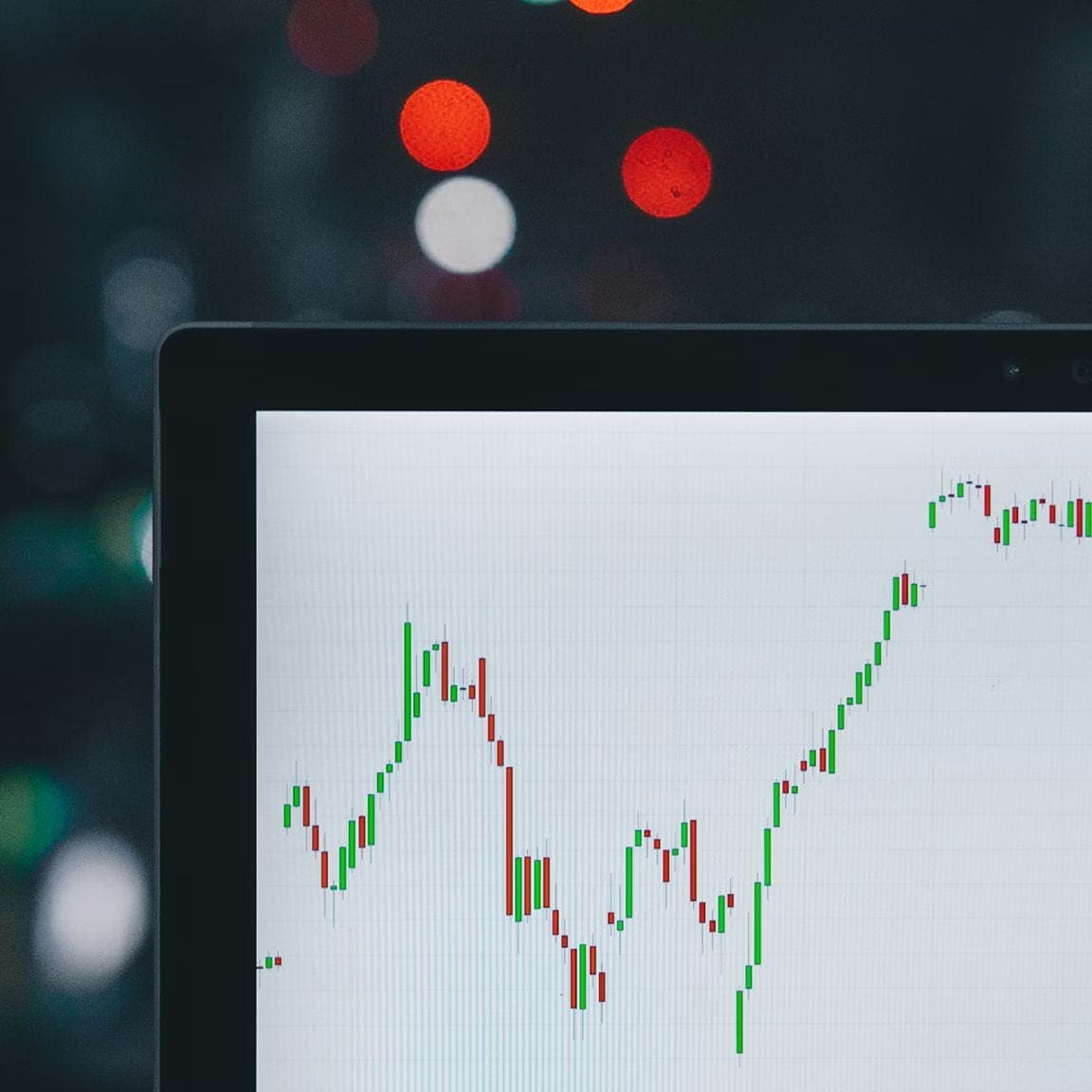 Laptop screen showing a candlestick chart with blurred lights behind it