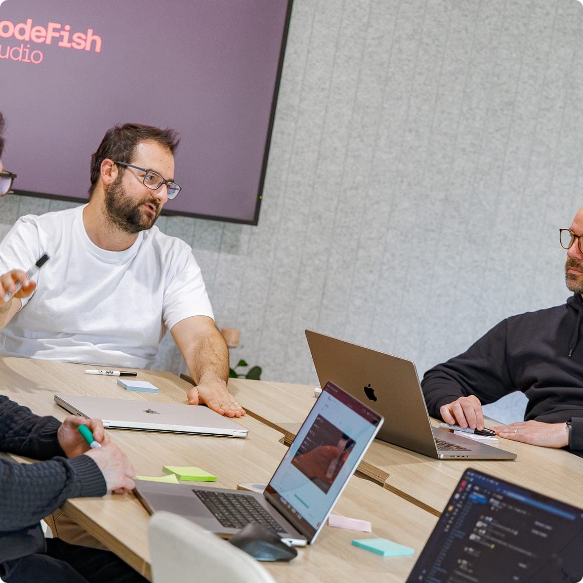 Four CodeFish team members working through a problem around a table of laptops, CodeFish Studio sign on the wall