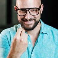 A smiling team member wearing glasses and a turquoise linen shirt