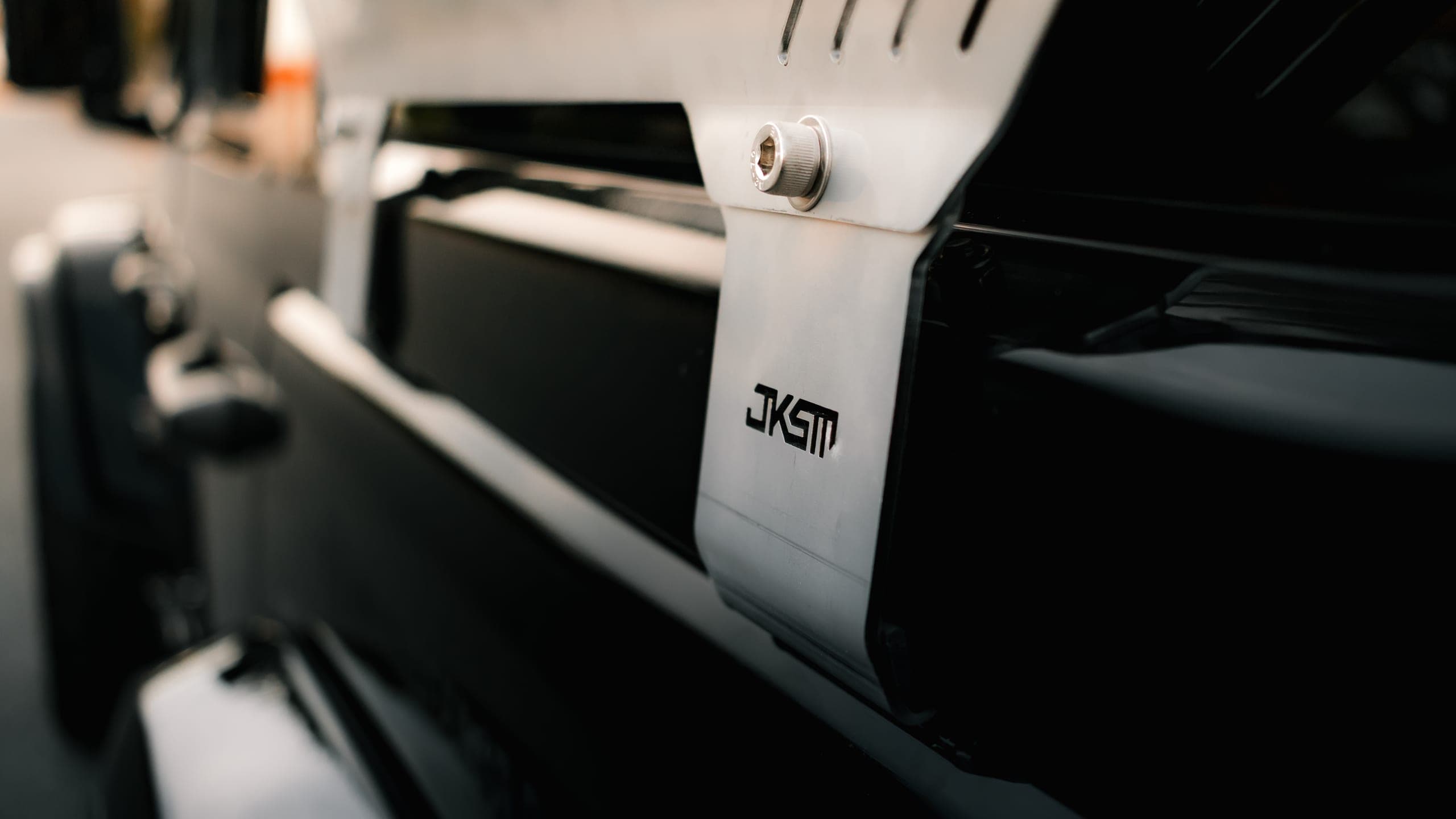Close-up of a JKSM logo etched into a brushed alloy vehicle mounting bracket