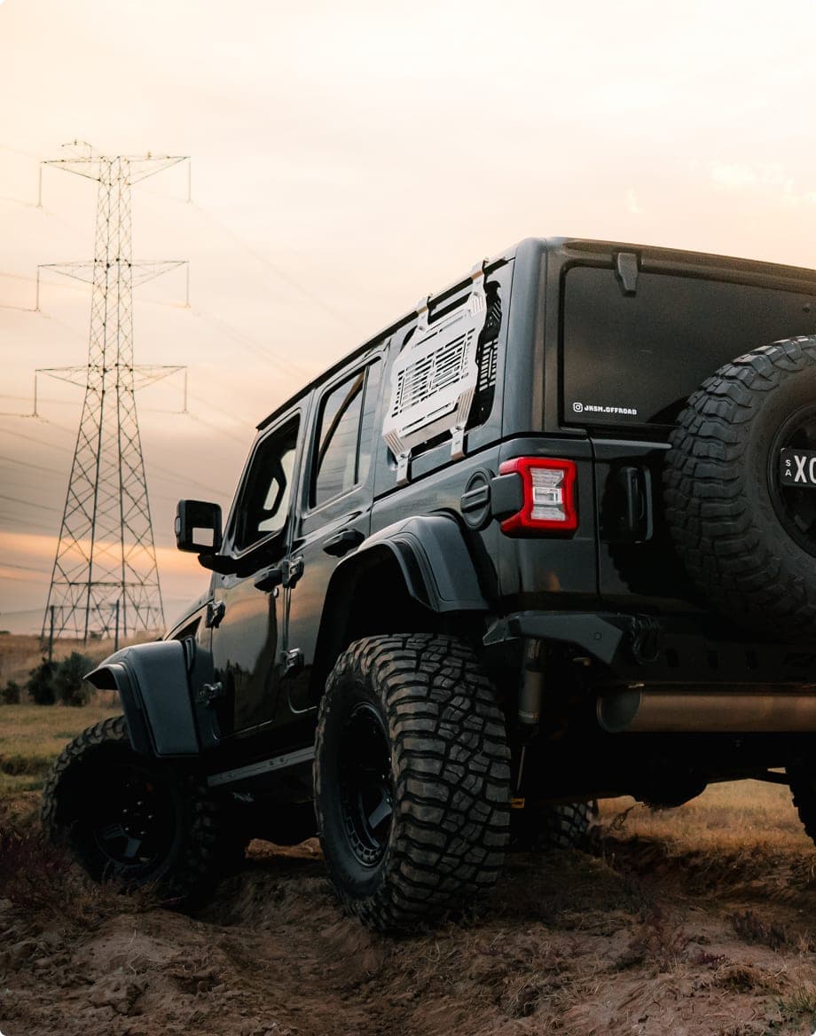 Lifted four-wheel drive with a slotted window storage panel parked in a paddock at sunset