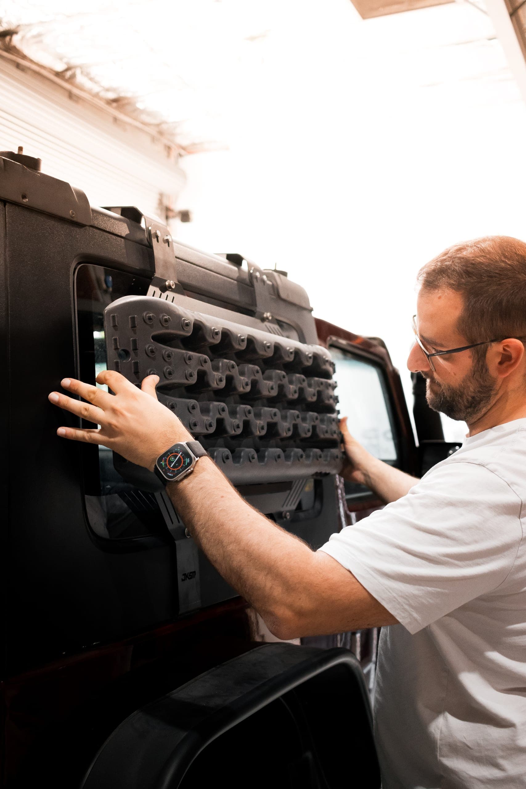 A team member fitting recovery tracks onto a window-mounted storage panel in a workshop