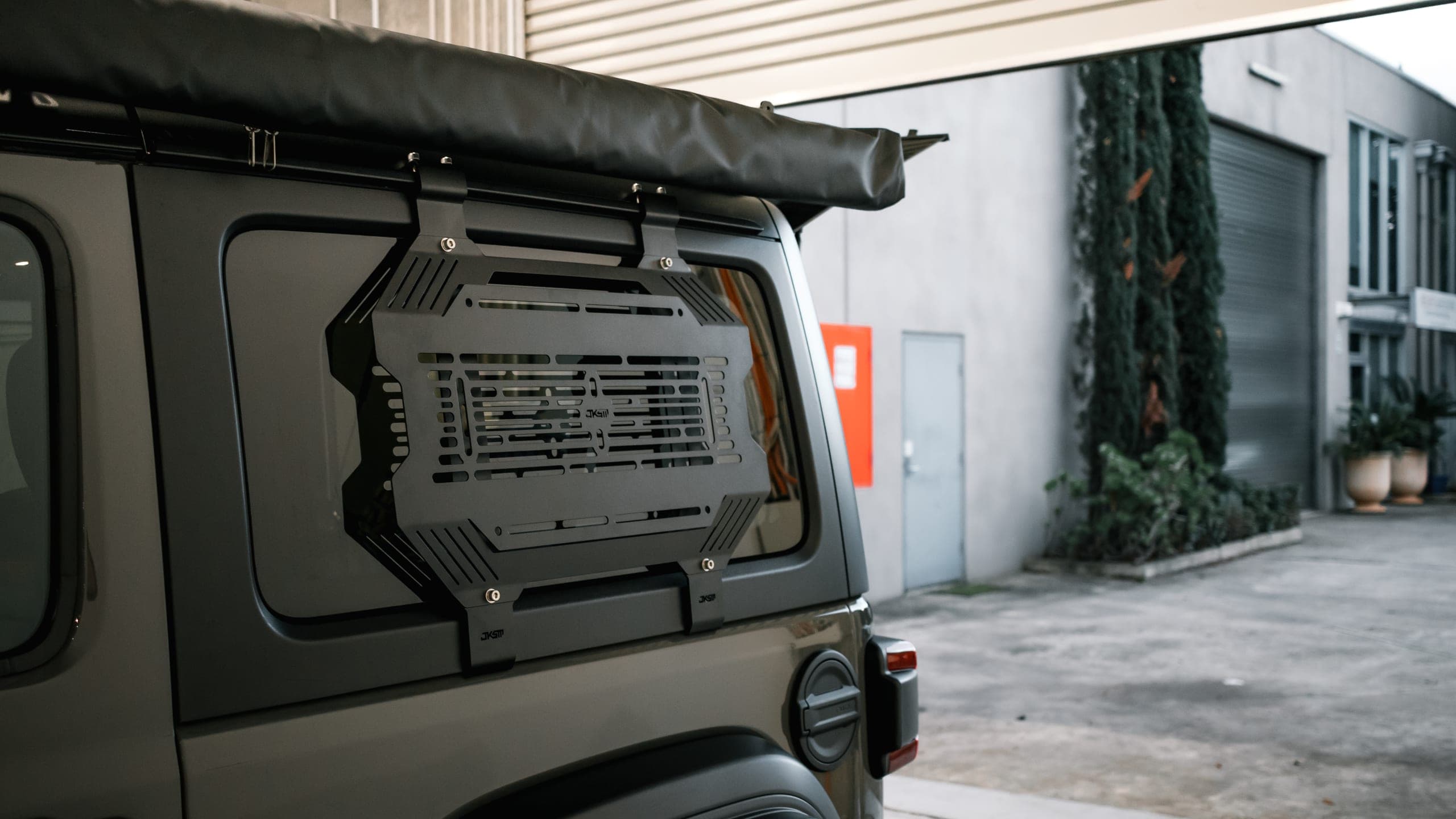 Raw alloy storage panel fitted to a four-wheel drive rear window outside an industrial workshop