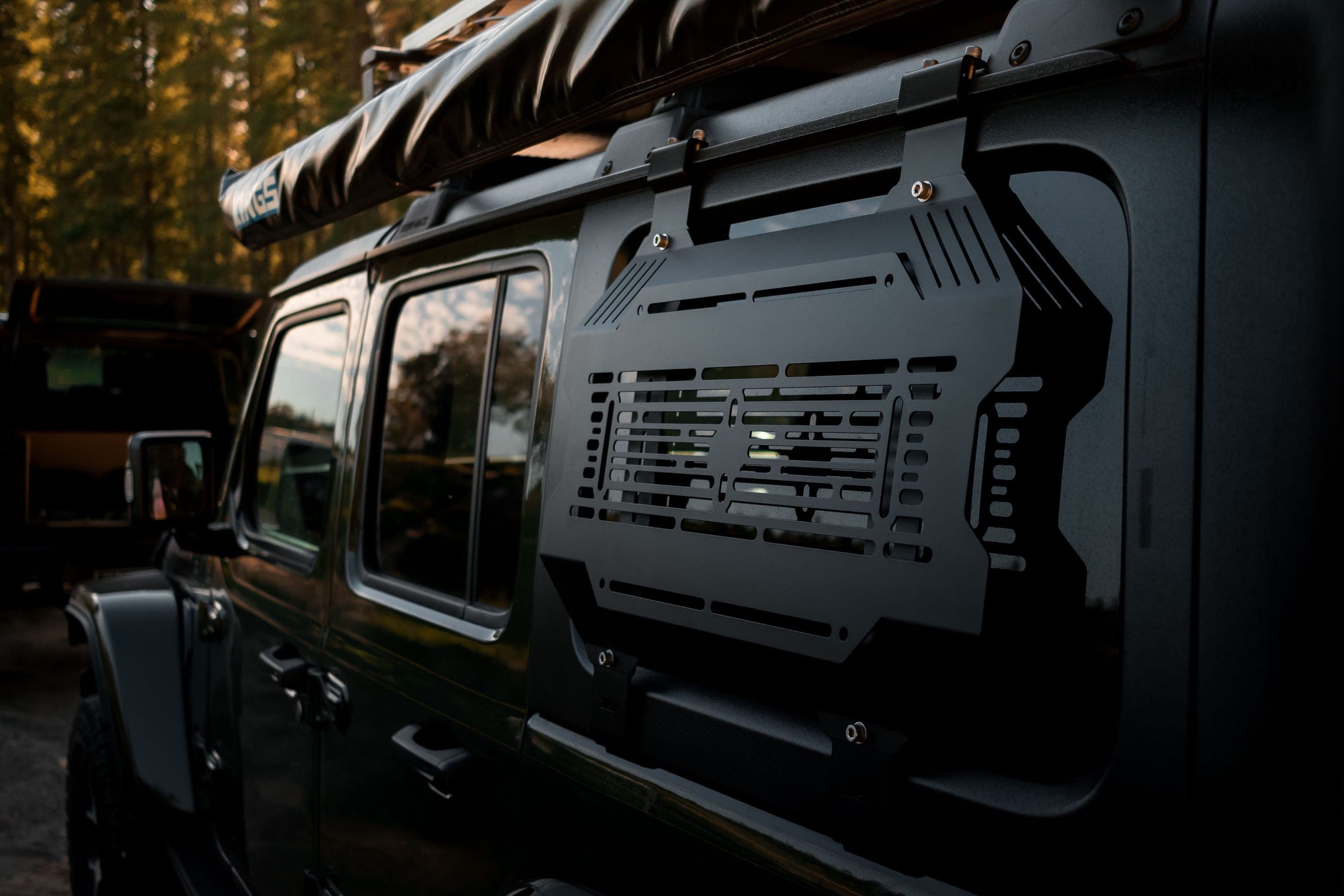 Slotted alloy storage panel mounted over a four-wheel drive rear window with a roof awning above
